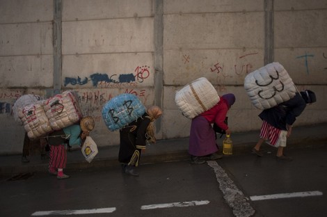 TO GO WITH AFP STORY BY ROLAND LLOYD PARRY AND INGRID BAZINET - Women porters carry bundles on their backs for transport across the El Tarajal boarder separating Morocco and Spain's North African enclave of Ceuta, in Ceuta on December 4, 2014. Unemployment among Ceuta and Melilla's native workforce is more than 30 percent -- among the highest rates in Spain. Meanwhile, authorities say some 30,000 Moroccan traders and menial workers cross into each territory every day. AFP PHOTO / JORGE GUERRERO